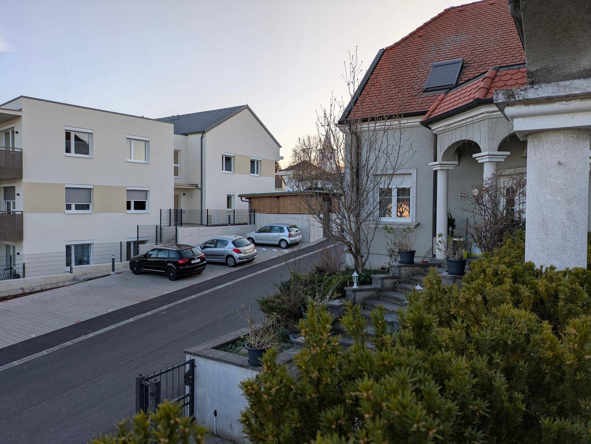 Blick auf die ruhige Wohnstraße mit benachbarten Gebäuden und geparkten Autos.