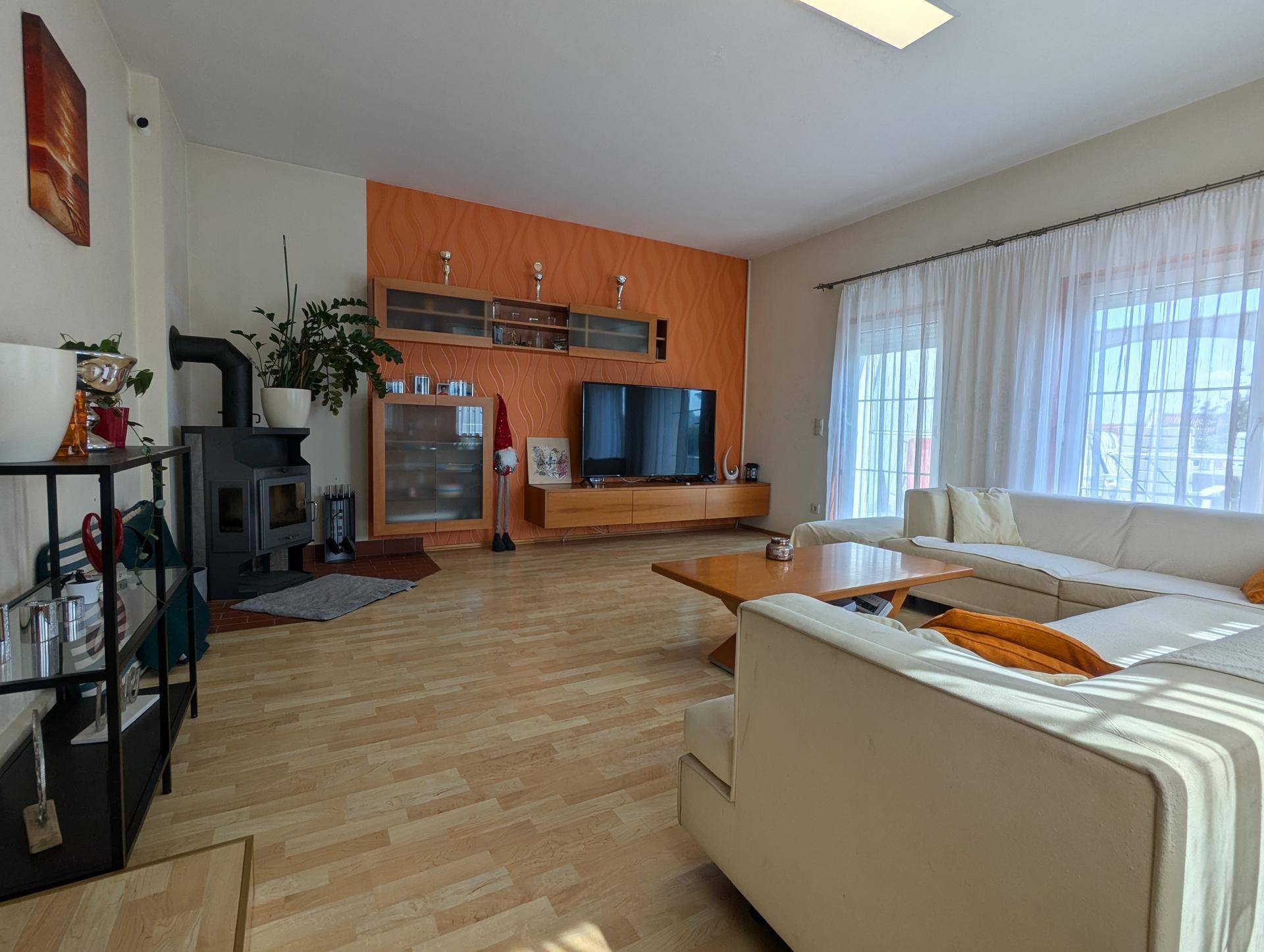 Geräumiges Wohnzimmer mit hellem Holzboden, Kaminofen und großen Fenstern zum Garten.