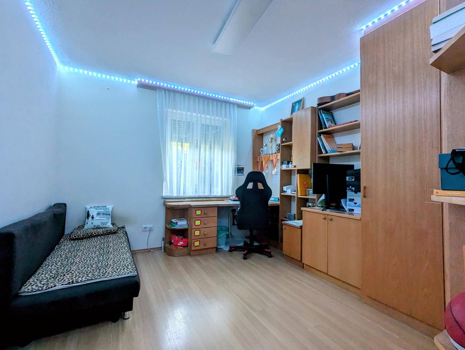 Jugendzimmer mit Schreibtisch, Regalen und dekorativer LED-Beleuchtung an der Decke.