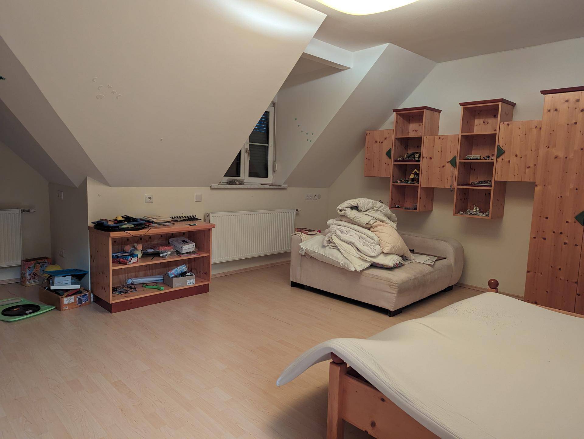 Dachgeschoss-Schlafzimmer mit schrägen Decken, Stauraum und hellem Laminatboden.