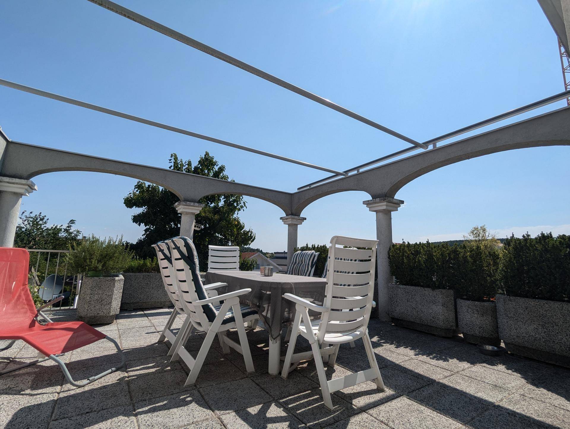 Sonnige Terrasse mit Pergola-Struktur, Gartenmöbeln und weitem Blick über die Umgebung.