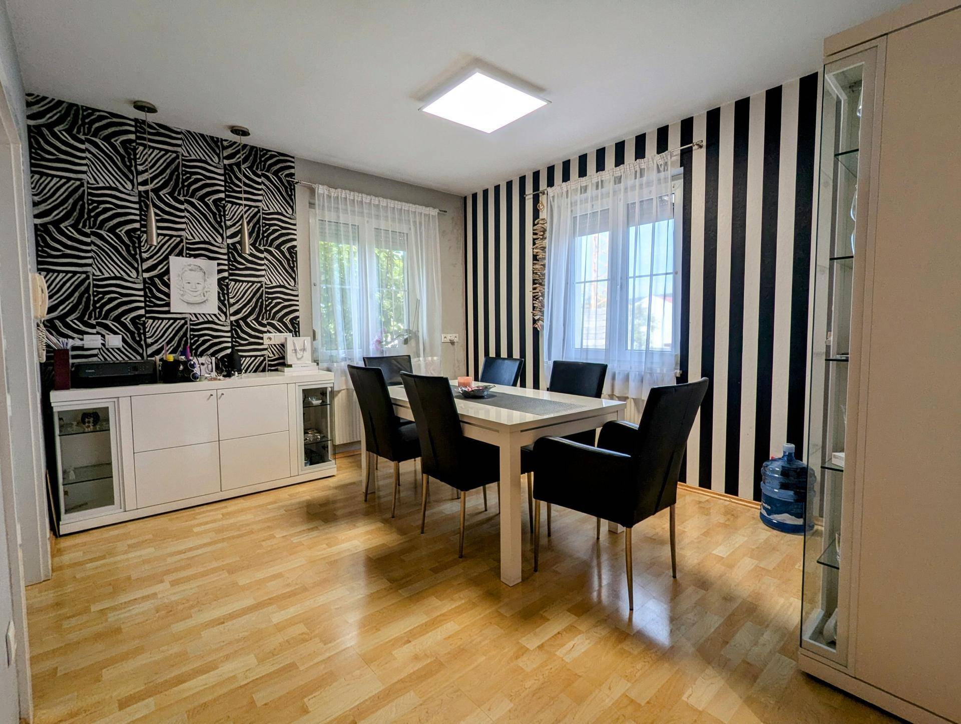 Helles Esszimmer mit Holzboden, modernem Esstisch und auffälliger schwarz-weißer Tapete.