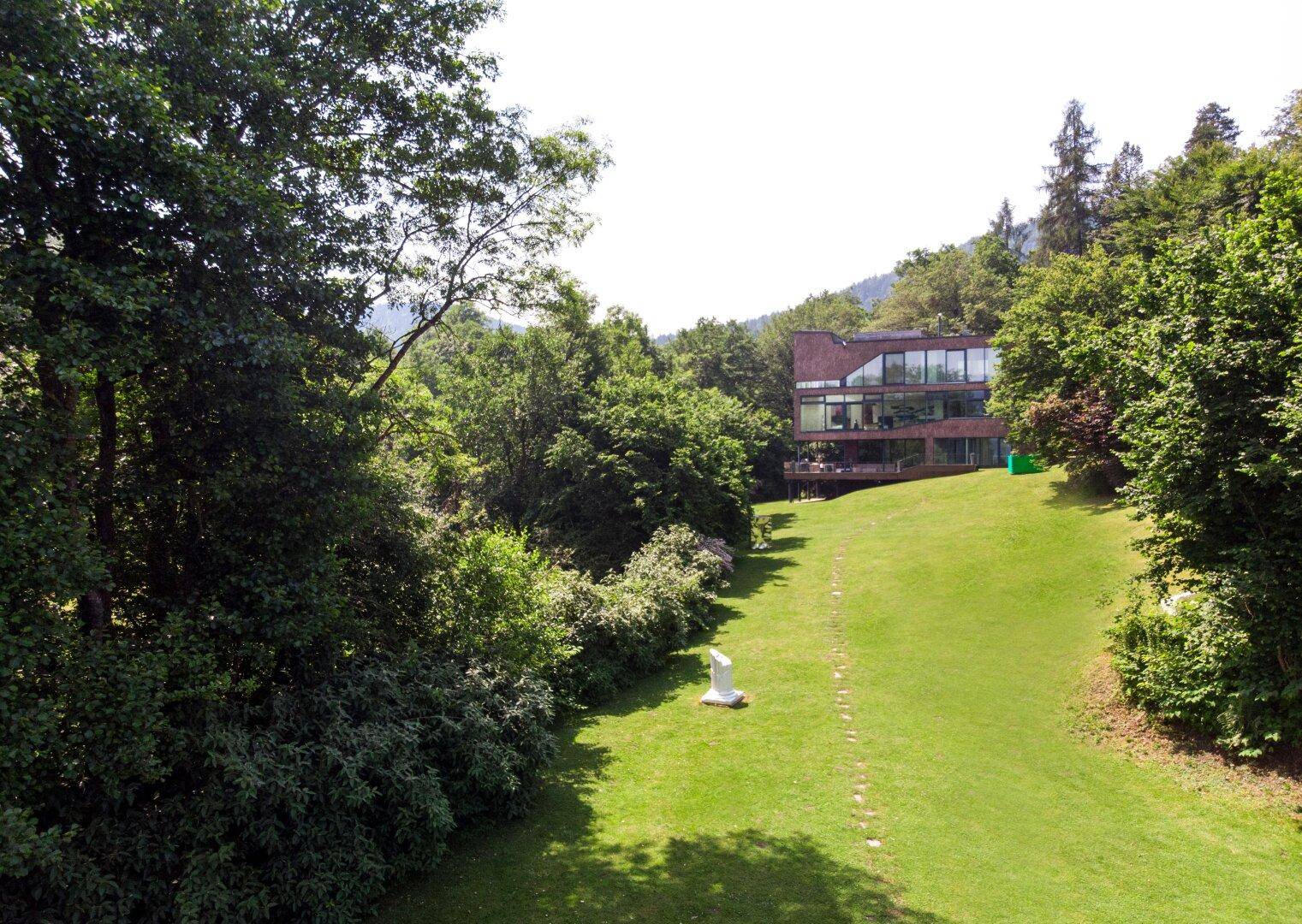 Weitläufiger Gartenbereich mit Blick auf das moderne Wohnhaus, eingebettet in grüne Hügellandschaft.