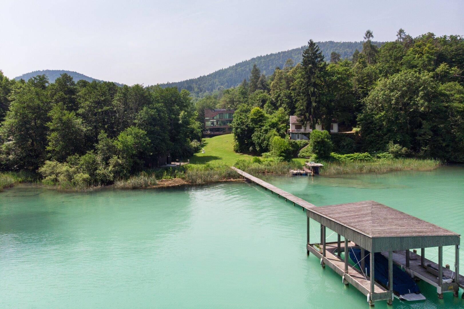 Malerischer Blick auf den türkisblauen See mit Bootssteg und bewaldeten Ufern in der Ferne.