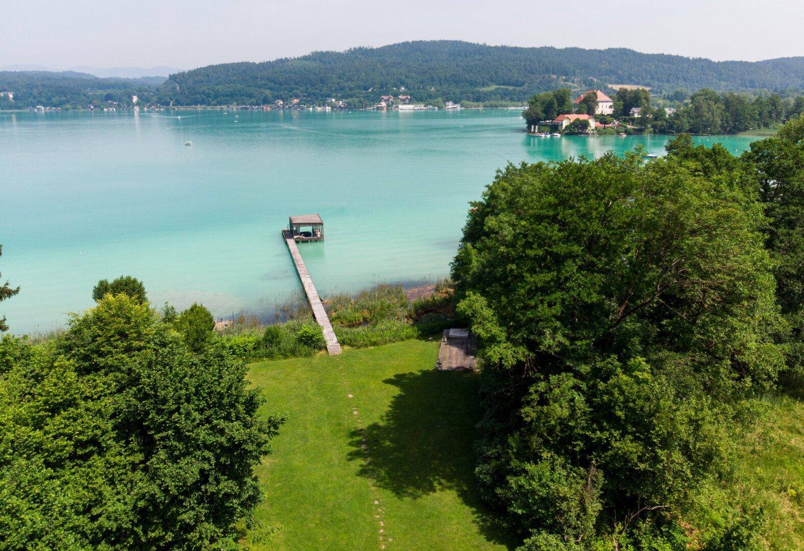 Panoramablick über den glitzernden See mit einem Bootssteg und einer Insel in der Ferne.
