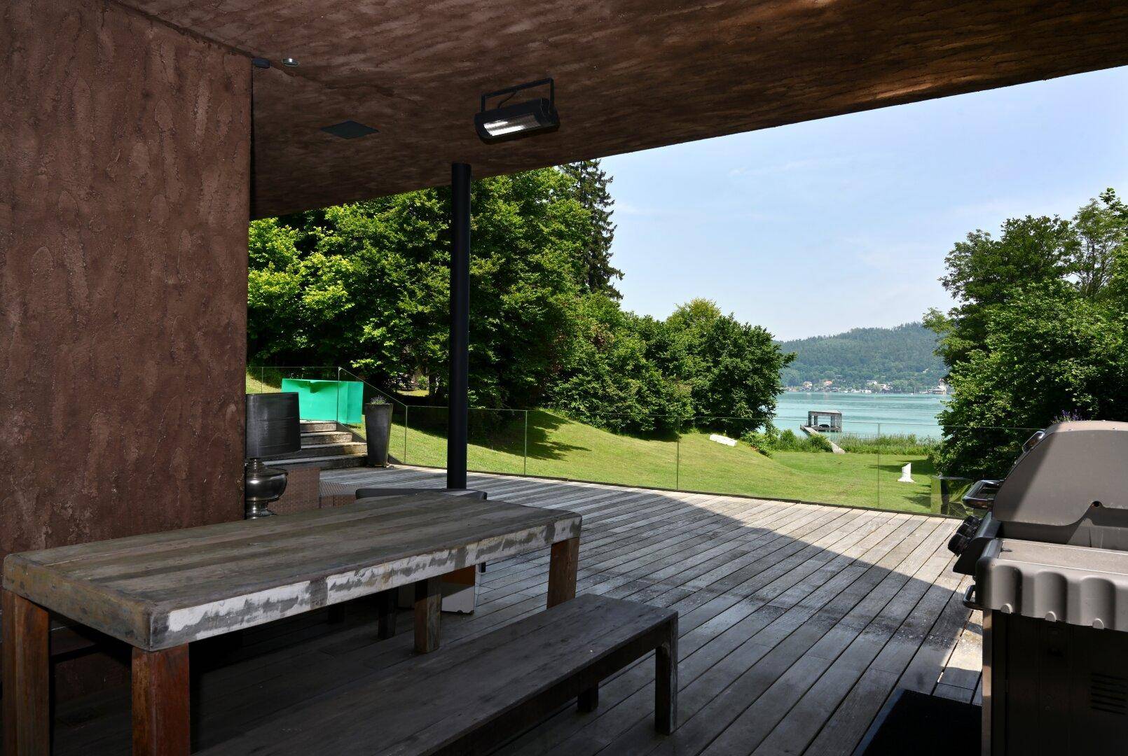 Überdachte Holzterrasse mit Esstisch und Grillbereich, bietet einen schönen Blick auf den See.