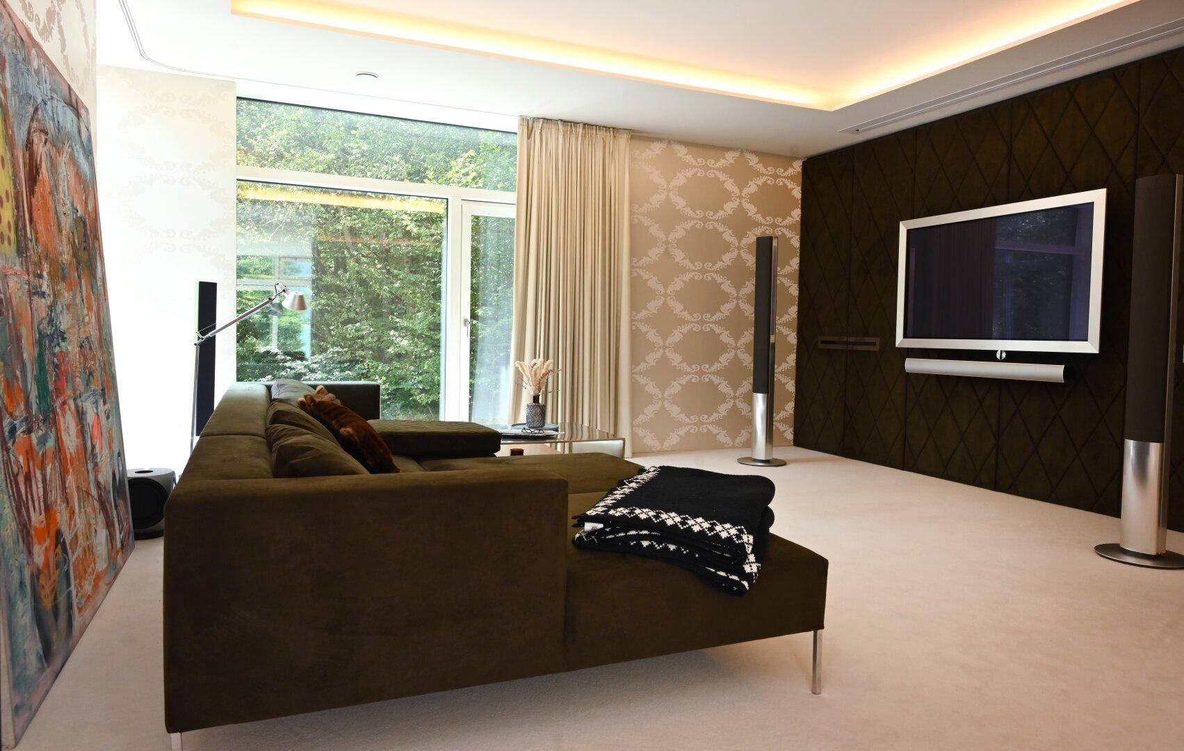 Gemütliches Wohnzimmer mit großem Sofa, Wandfernseher und dekorativer Tapete, hell durch Fenster.
