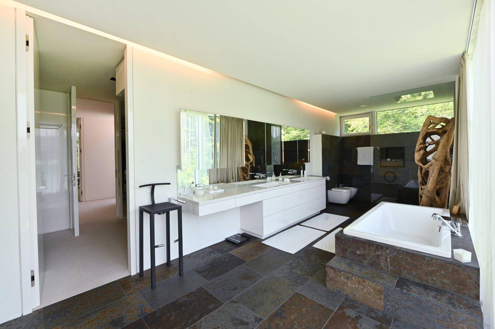 Modernes Badezimmer mit Doppelwaschbecken, Badewanne und Natursteinboden, hell und geräumig.