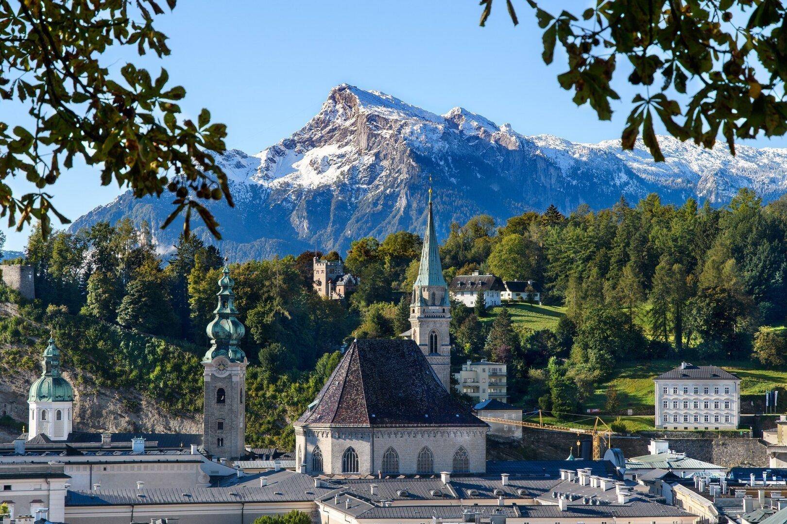 Malerischer Blick auf eine Stadt mit historischen Gebäuden und schneebedeckten Bergen im Hintergrund.