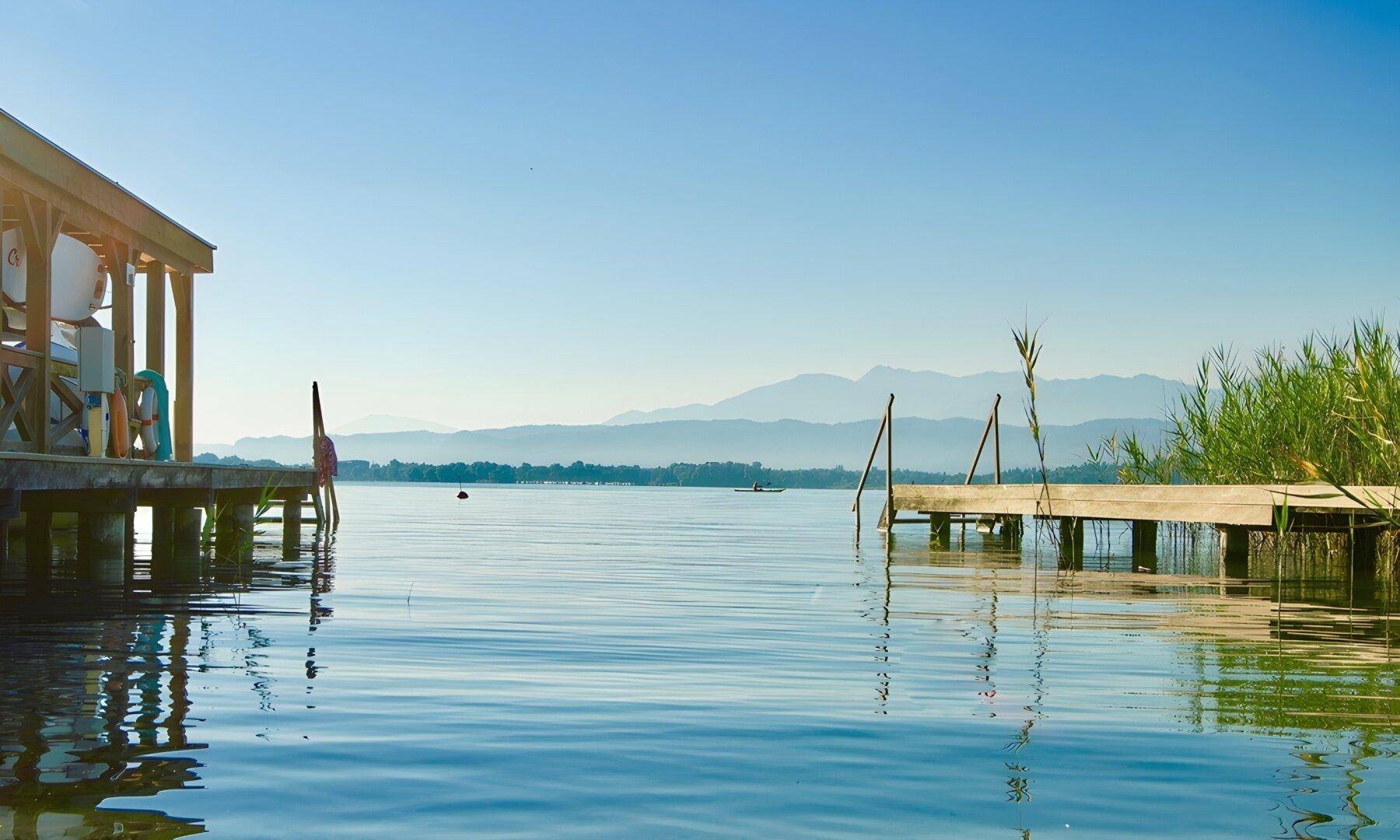 Ruhiger See mit Holzstegen und Bergen im Hintergrund unter klarem Himmel.