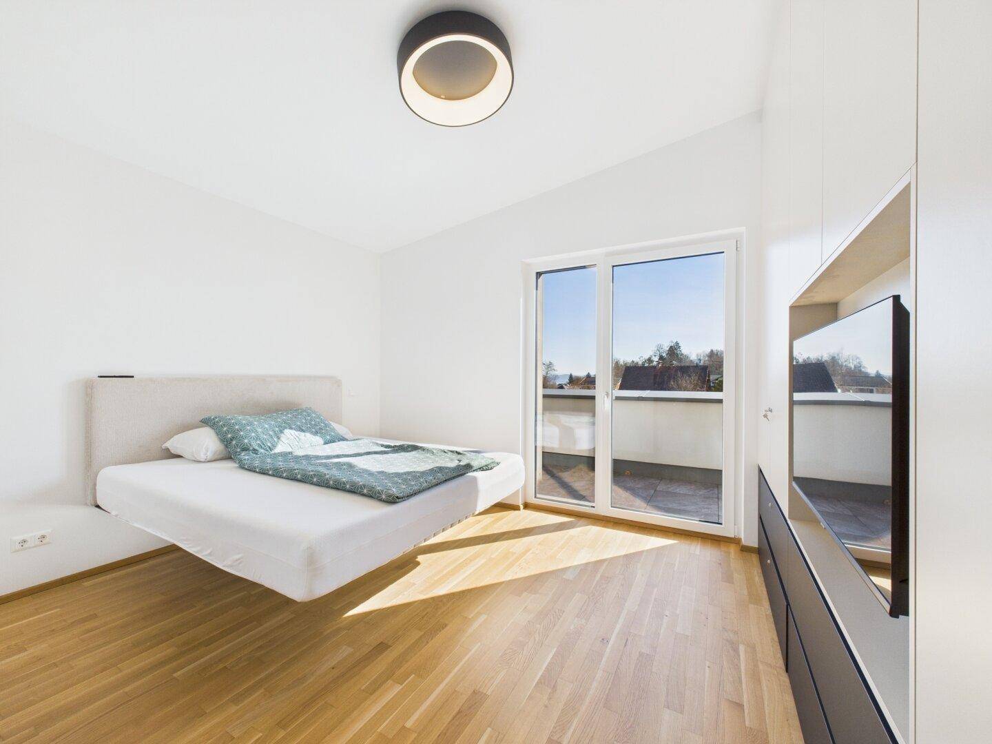 Helles Schlafzimmer mit schwebendem Bett, Holzboden und direktem Zugang zur Terrasse.