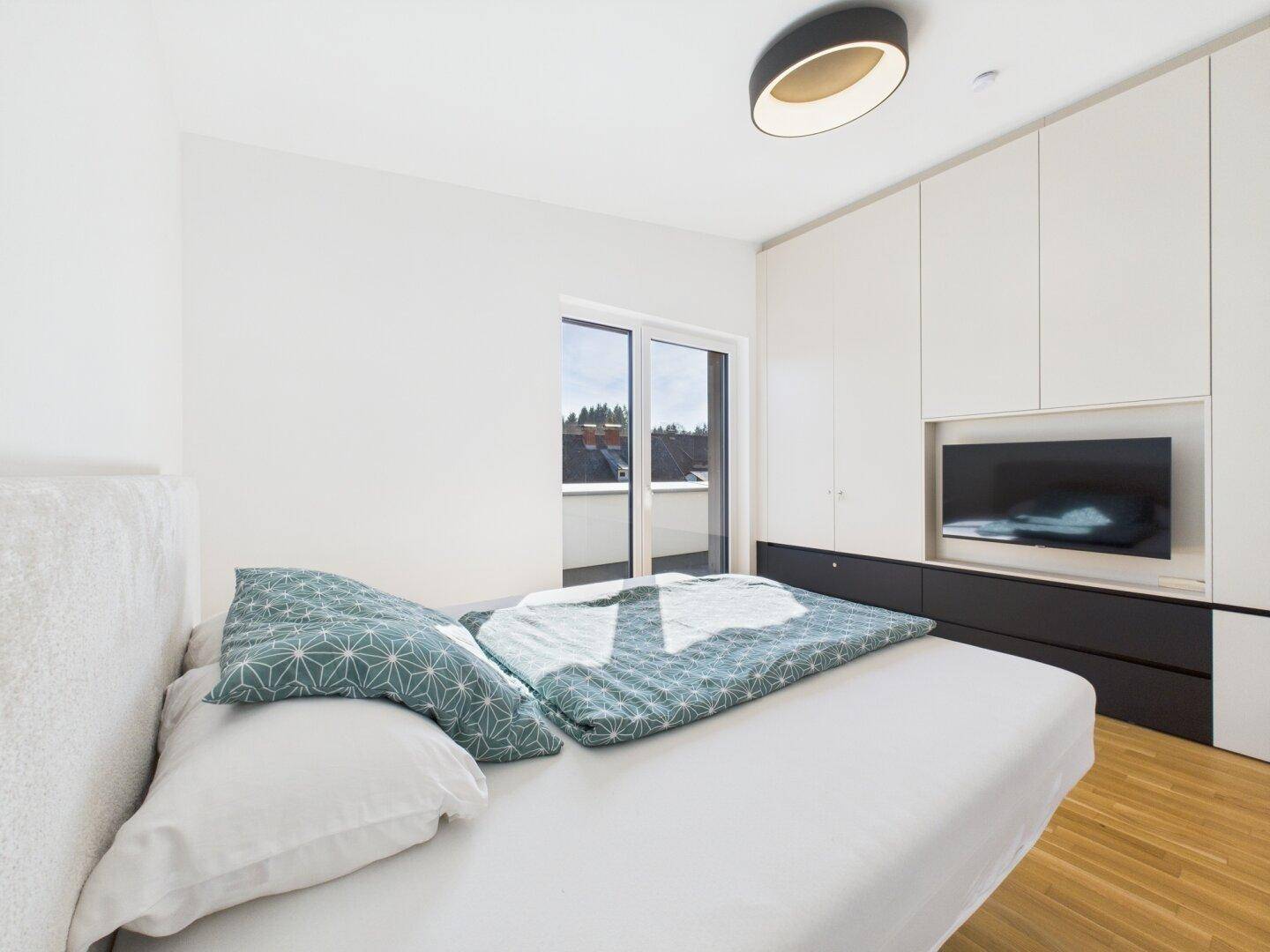 Schlafzimmer mit integriertem Wandschrank, Fernseher und Zugang zur sonnigen Terrasse.