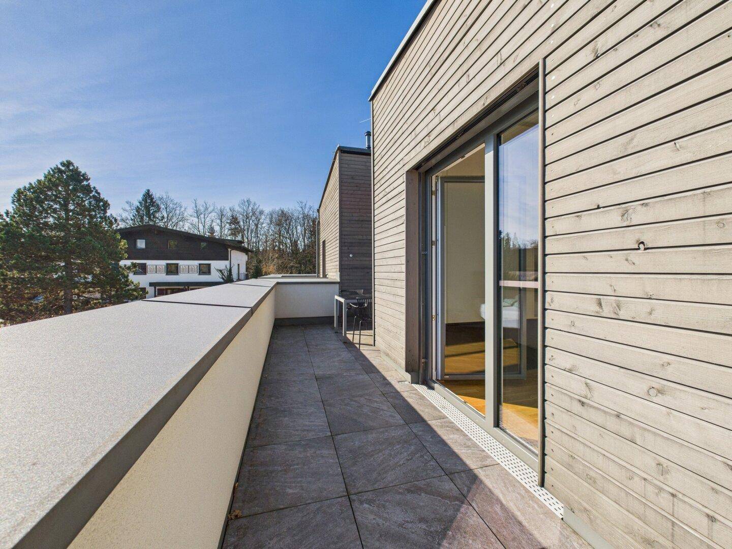 Langer Balkon mit Holzwänden, Fliesenboden und weitem Blick in die Umgebung.