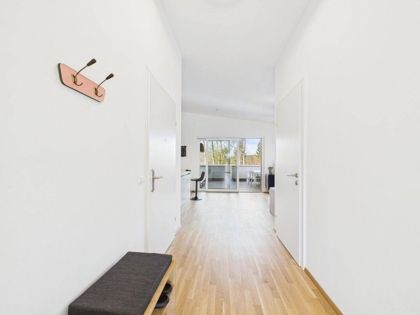 Heller Flur mit Holzfußboden, Garderobe und offenem Blick in den Wohnbereich.