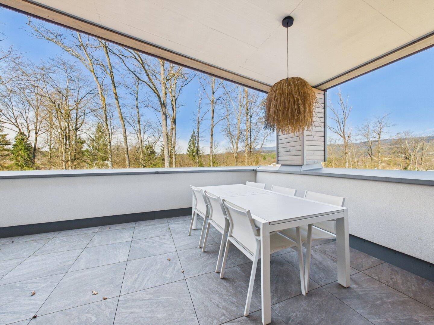 Überdachte Terrasse mit Essbereich, Fliesenboden und weitem Blick in die Natur.
