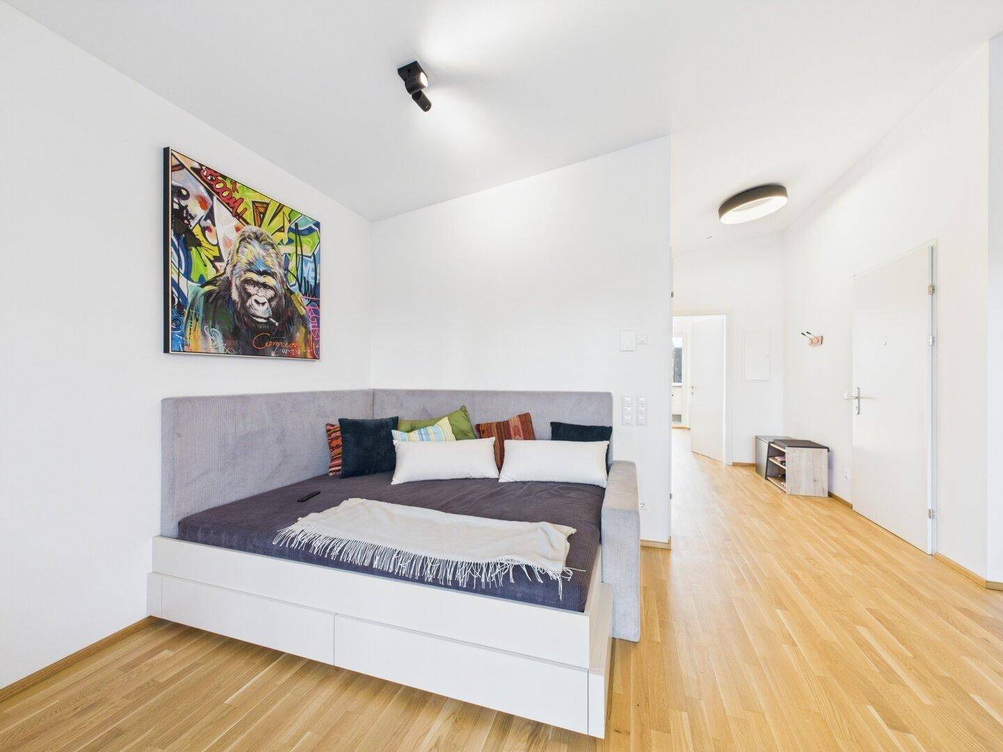 Schlafzimmer mit Tagesbett, farbenfrohem Kunstwerk und hellem Holzfußboden.