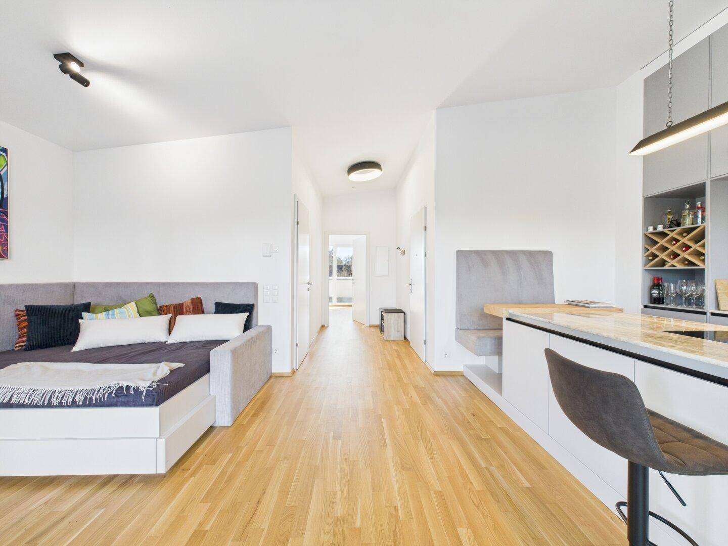 Offener Wohnbereich mit Tagesbett, Holzboden und Blick zur modernen Küche.
