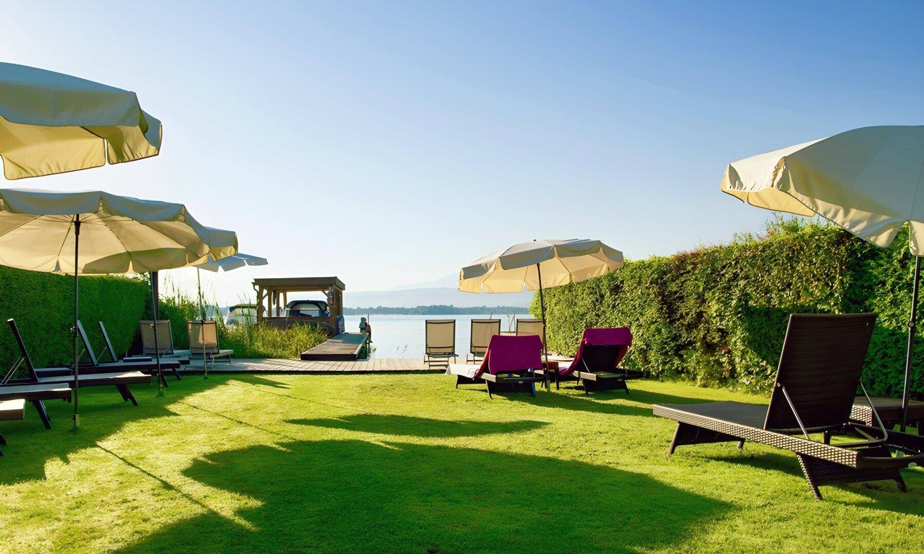 Gepflegte Rasenfläche mit Liegestühlen und Sonnenschirmen direkt am Seeufer mit Bergblick.