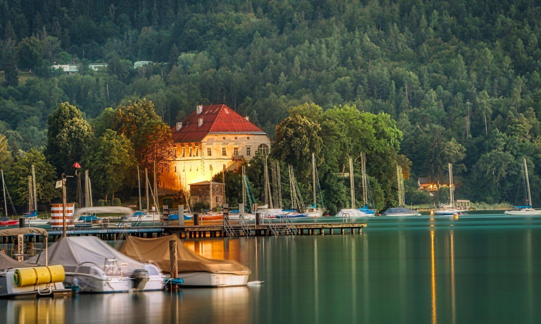 Malerischer Blick auf den See mit Yachthafen, Booten und einem historischen Gebäude am Ufer.