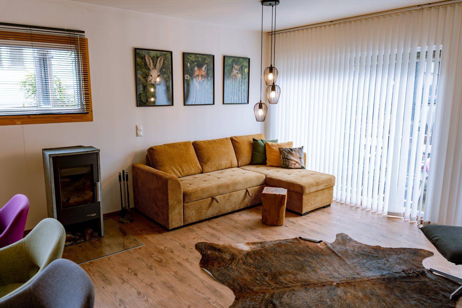 Helles Wohnzimmer mit bequemer Couch, Holzboden und Kaminofen für gemütliche Abende.