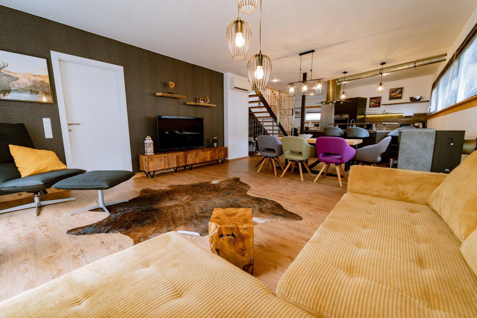 Offener Wohnbereich mit Sofa, Fernseher und Essbereich im Hintergrund.