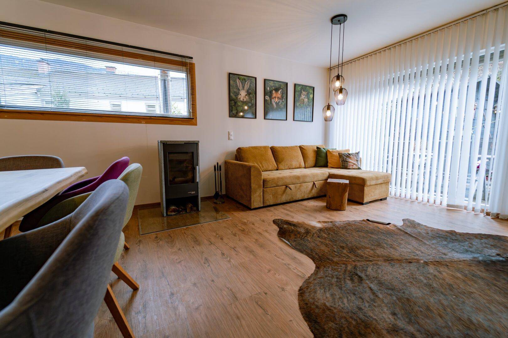 Gemütliches Wohnzimmer mit Sofa, Kaminofen und großen Fenstern für viel Licht.