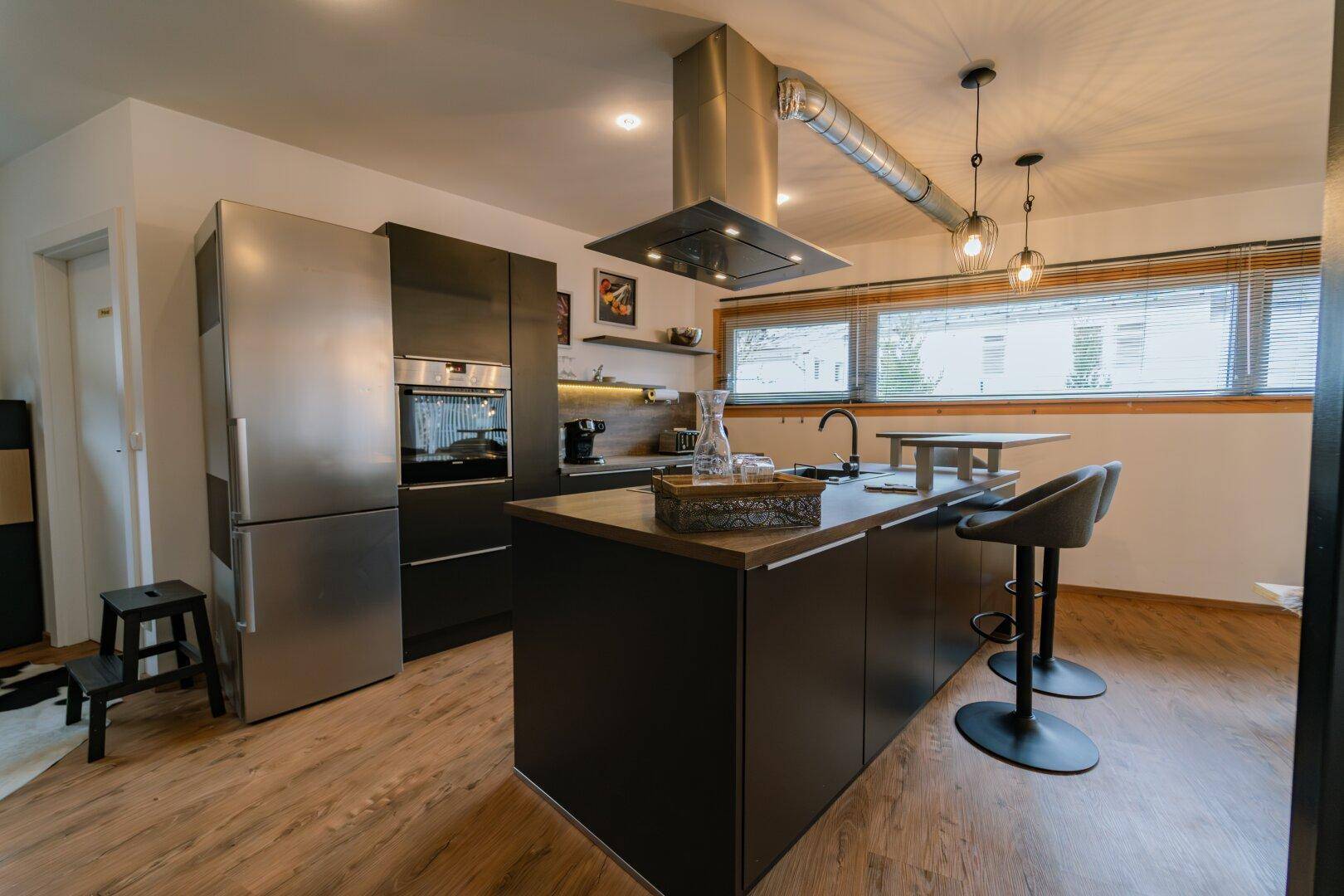 Moderne Küche mit Edelstahlkühlschrank, Kochinsel und Barhockern.