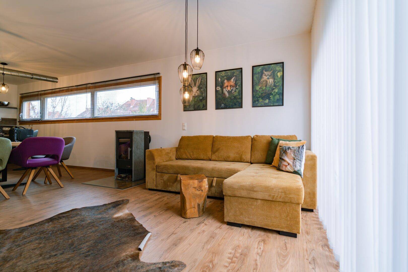 Helles Wohnzimmer mit bequemer Couch, Holzboden und Kaminofen.