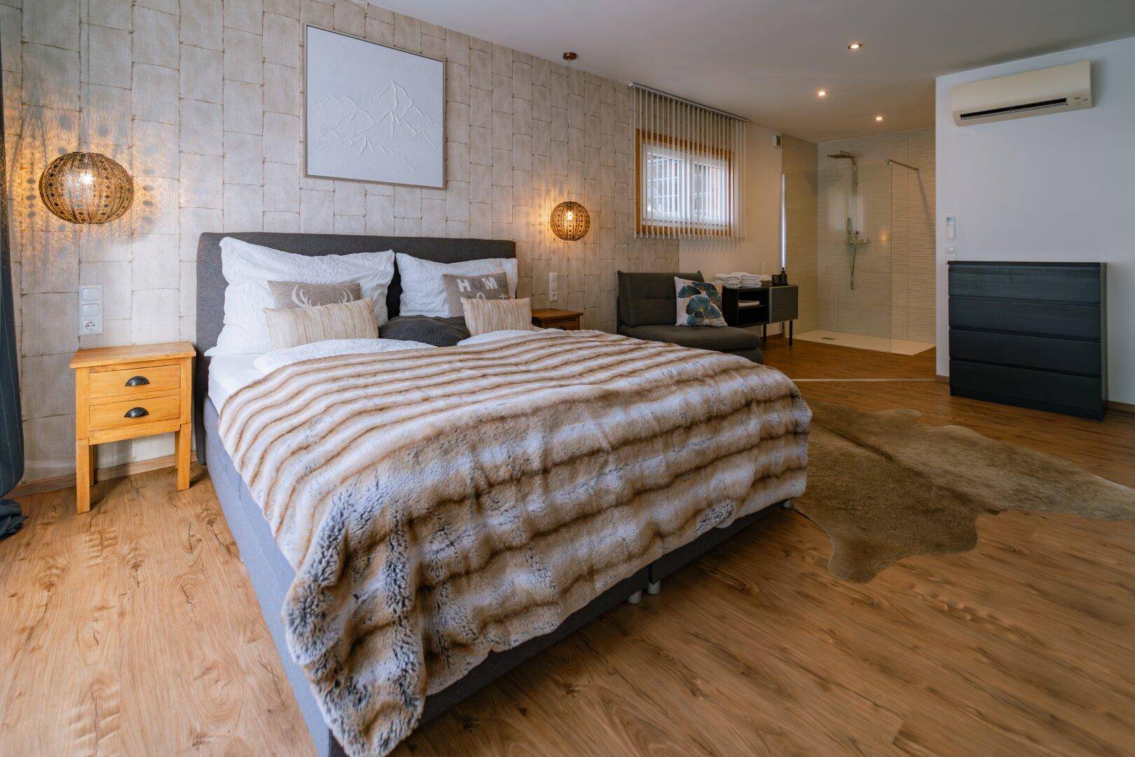 Helles Schlafzimmer mit großem Bett, Holzboden und integrierter Dusche.