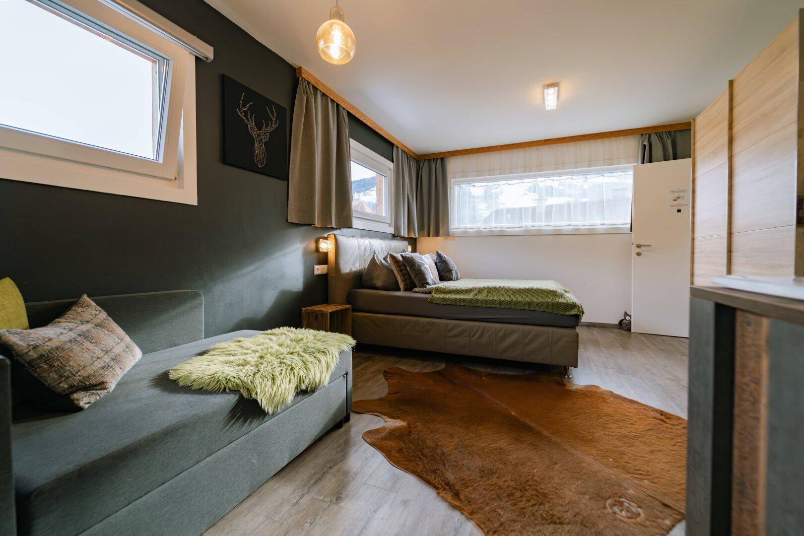 Schlafzimmer mit Doppelbett, Sofa und rustikalen Dekorationselementen.