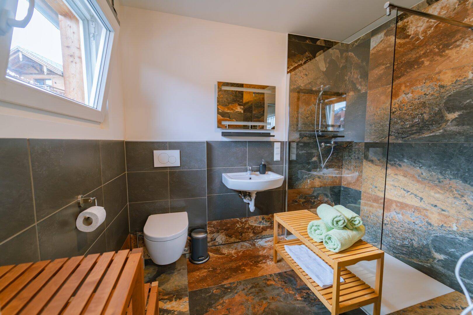 Modernes Badezimmer mit begehbarer Dusche und dunklen Natursteinfliesen.