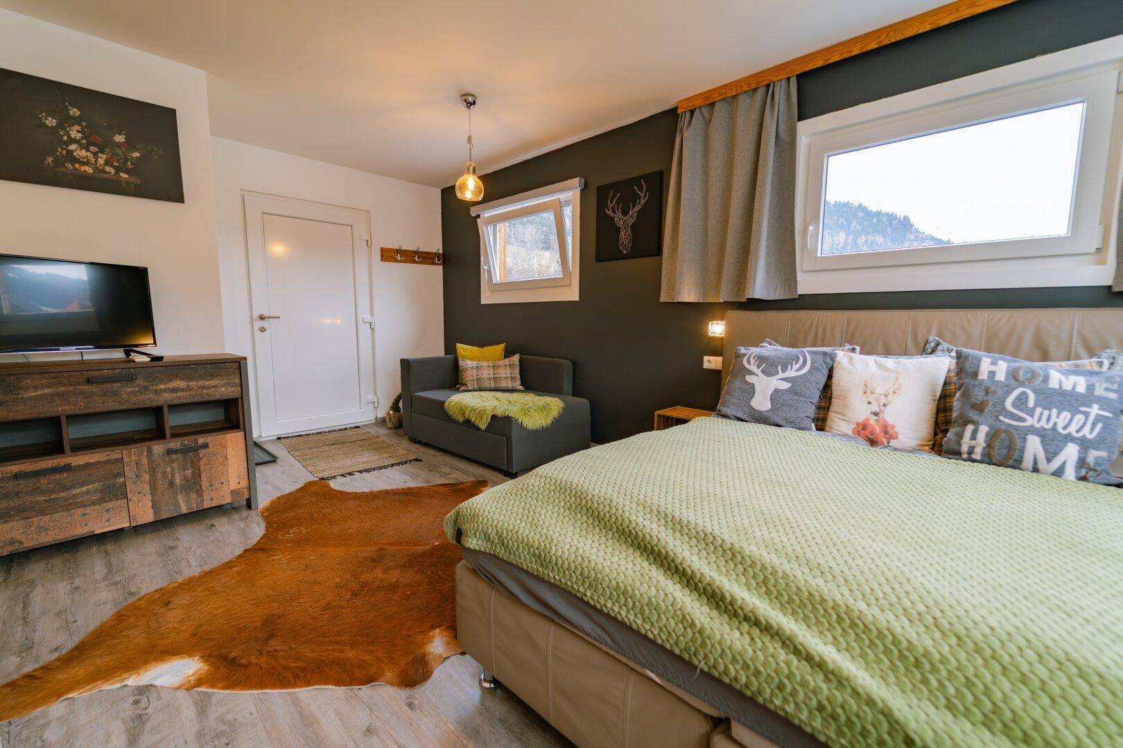 Schlafzimmer mit Doppelbett, Sofa und rustikalen Dekorationselementen.