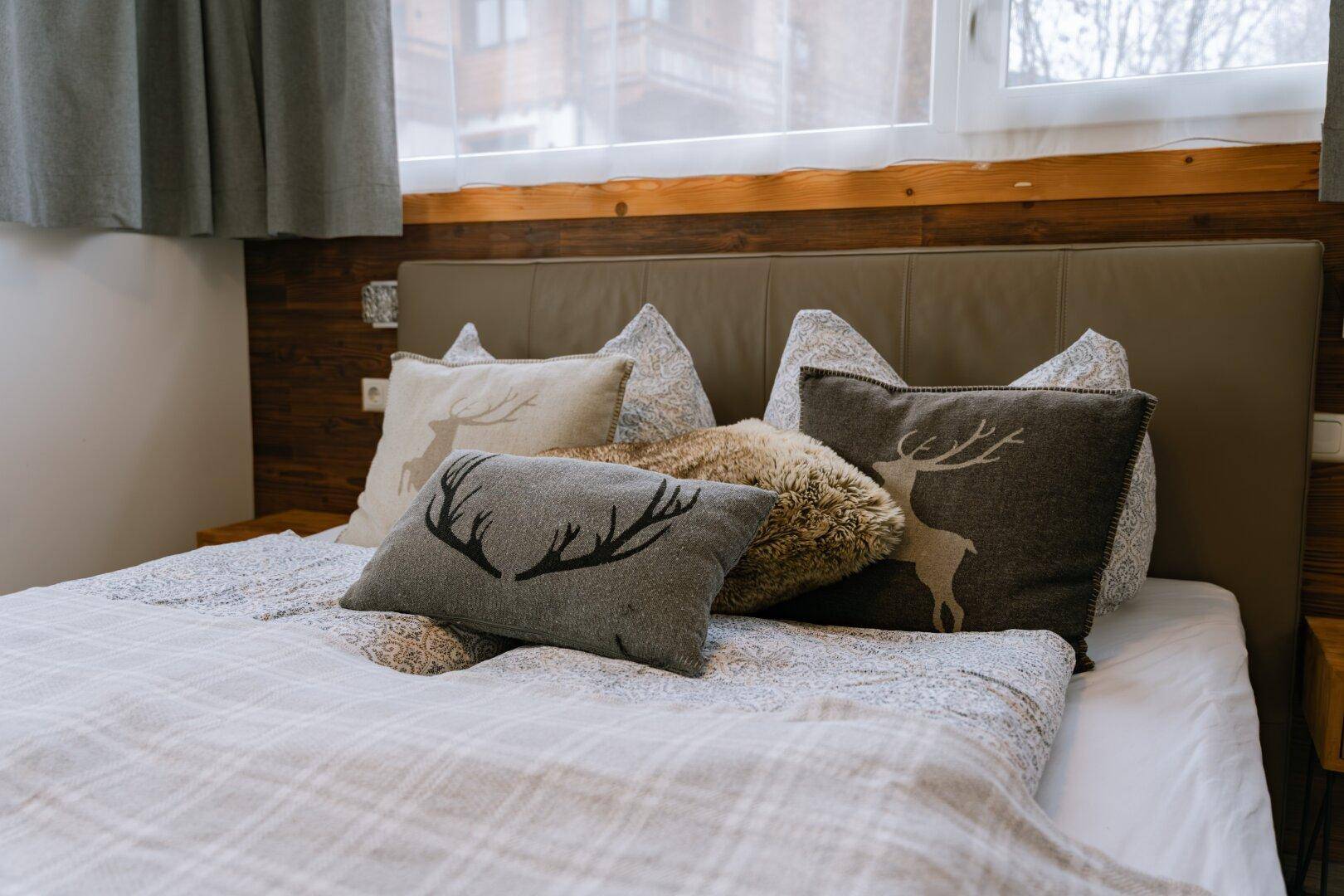 Schlafzimmer mit Doppelbett, Hirschkissen und rustikalen Holzakzenten.