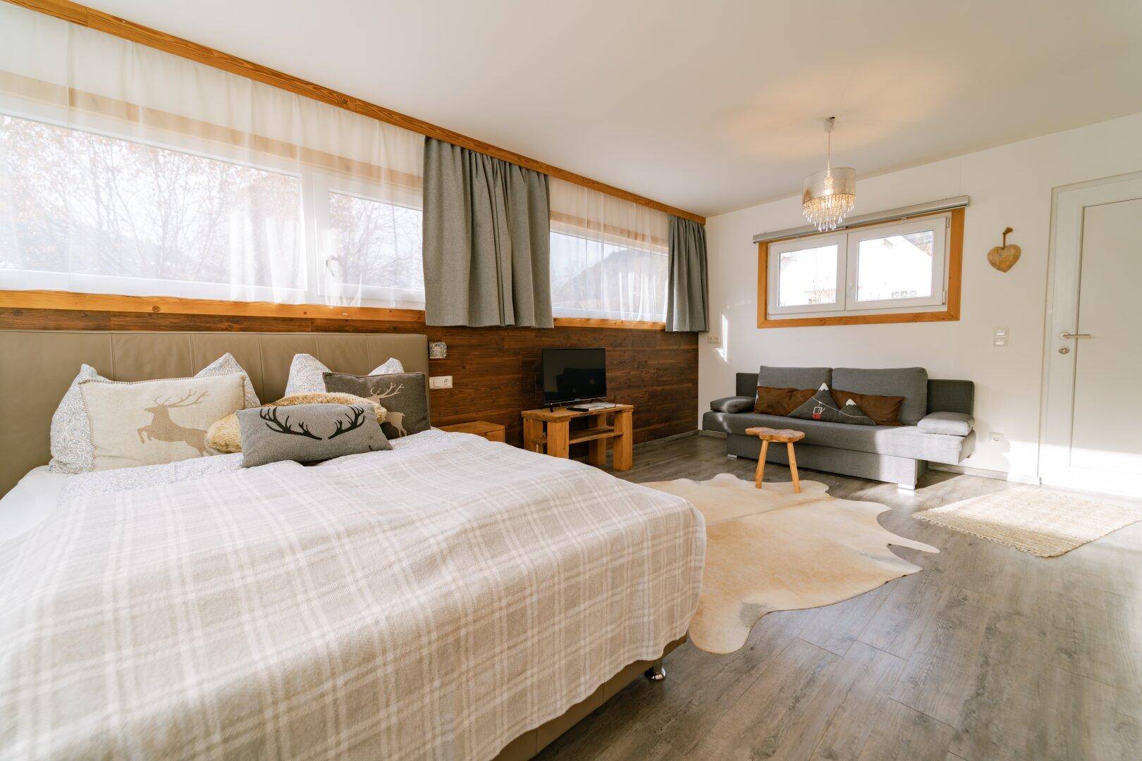 Helles Schlafzimmer mit Doppelbett, Sofa und Holzwandverkleidung.