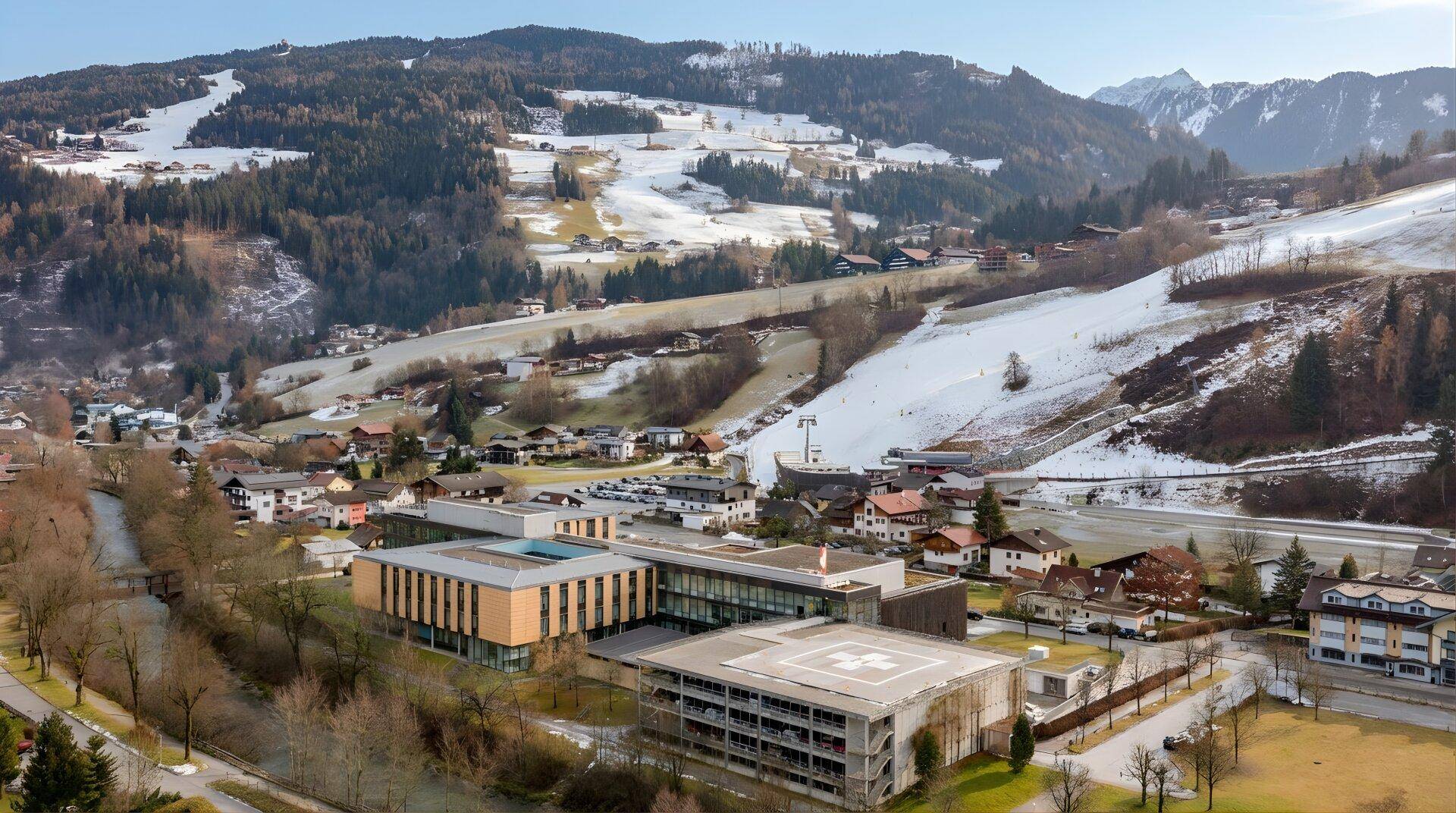 Luftaufnahme einer Stadt mit Gebäuden und schneebedeckten Bergen im Hintergrund.