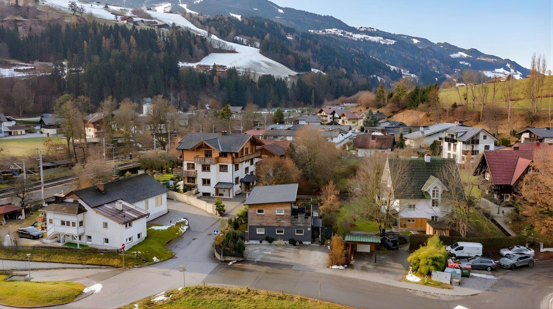 Weitläufige Luftaufnahme einer Siedlung mit Häusern und schneebedeckten Bergen.