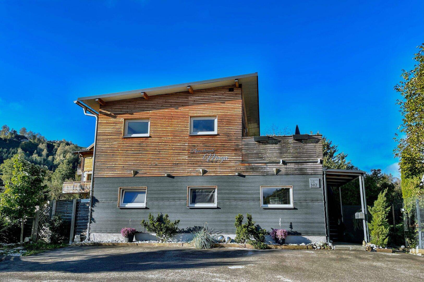 Modernes Gebäude mit Holzfassade, großen Fenstern und Carport.