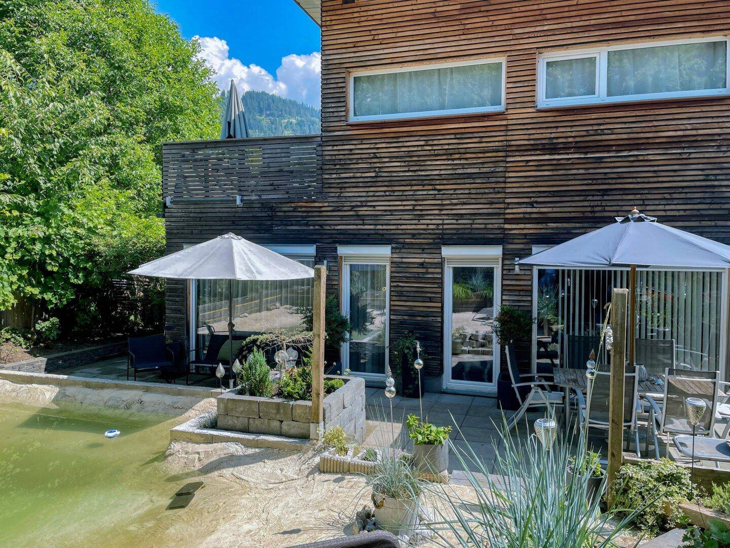 Sonniger Terrassenbereich mit Gartenmöbeln, Sonnenschirm und Teich.