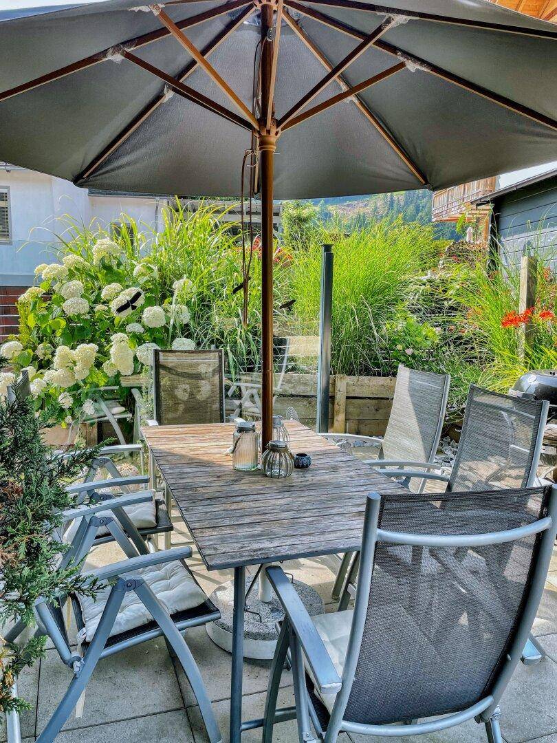 Gemütlicher Essbereich im Freien auf der Terrasse mit Sonnenschirm und Pflanzen.
