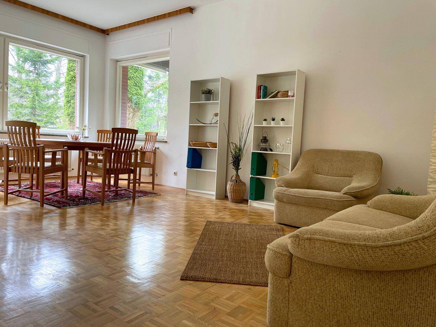 Heller Wohn- und Essbereich mit Holztisch, Stühlen und Regalen, Parkettboden und Blick ins Grüne.