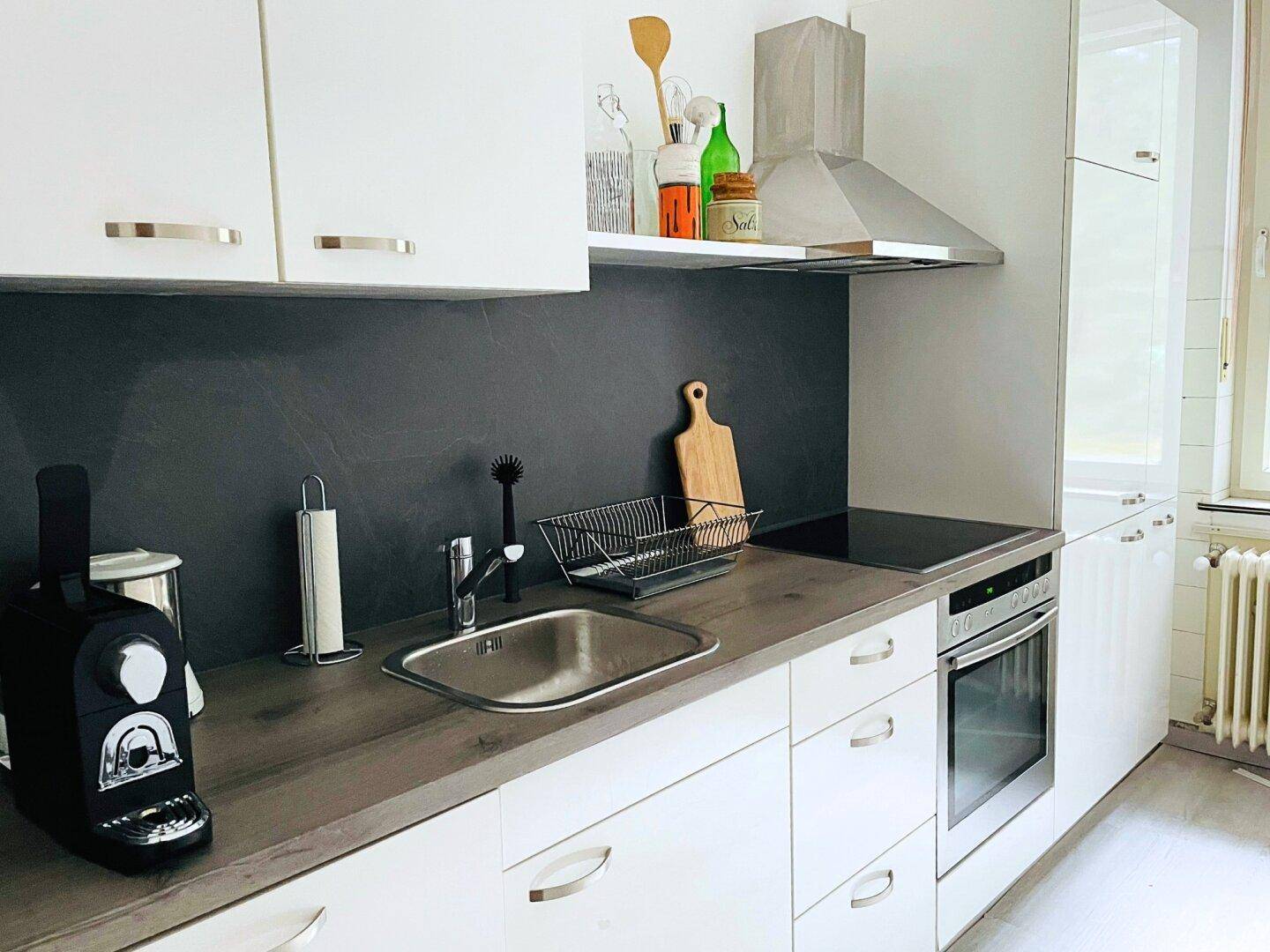 Moderne Einbauküche mit weißen Schränken, dunkler Arbeitsplatte und integrierten Geräten.