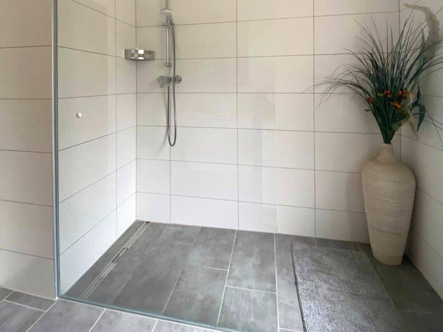 Modernes Badezimmer mit ebenerdiger Dusche, weißen Fliesen und grauen Bodenfliesen.