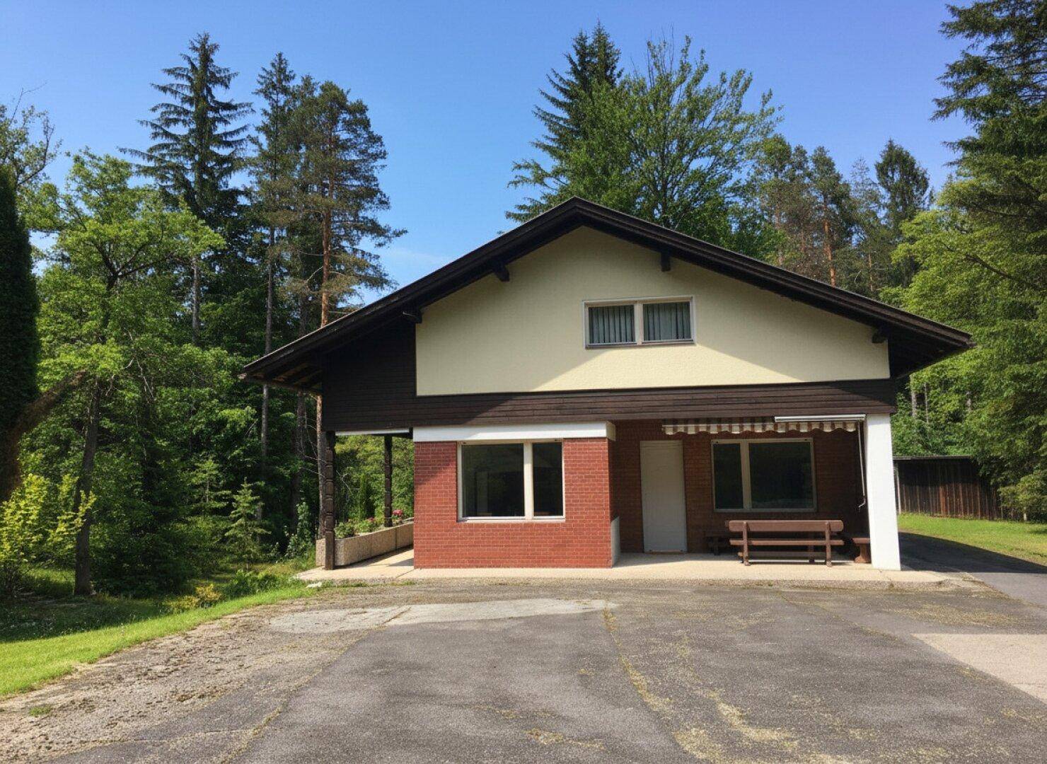 Vorderansicht eines Hauses mit roter Ziegelfassade und einem überdachten Eingangsbereich, umgeben von Bäumen.