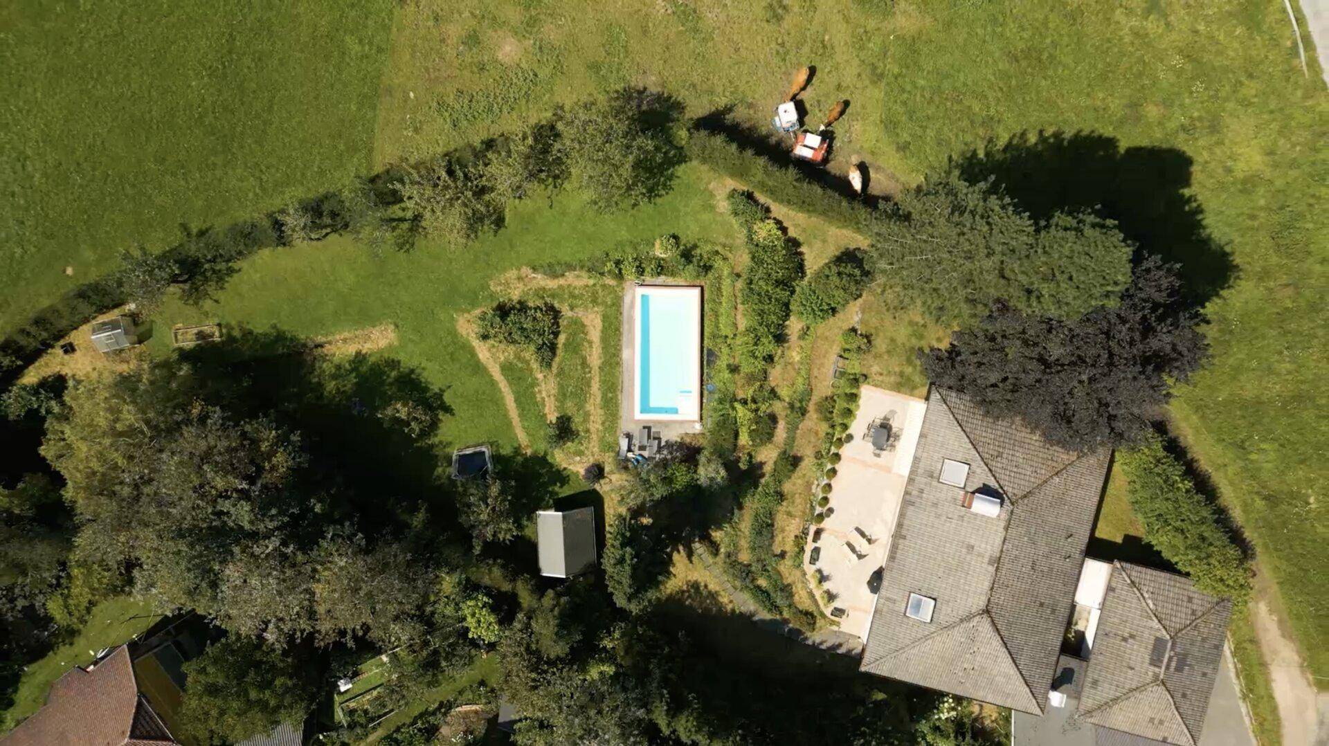 Luftaufnahme eines Anwesens mit Haus, rechteckigem Pool und weitläufigen Grünflächen.