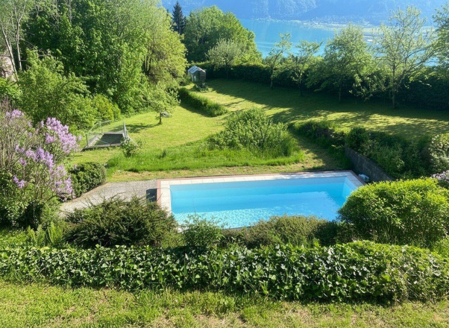 Gepflegter Gartenbereich mit rechteckigem Pool und Blick auf den See im Hintergrund.
