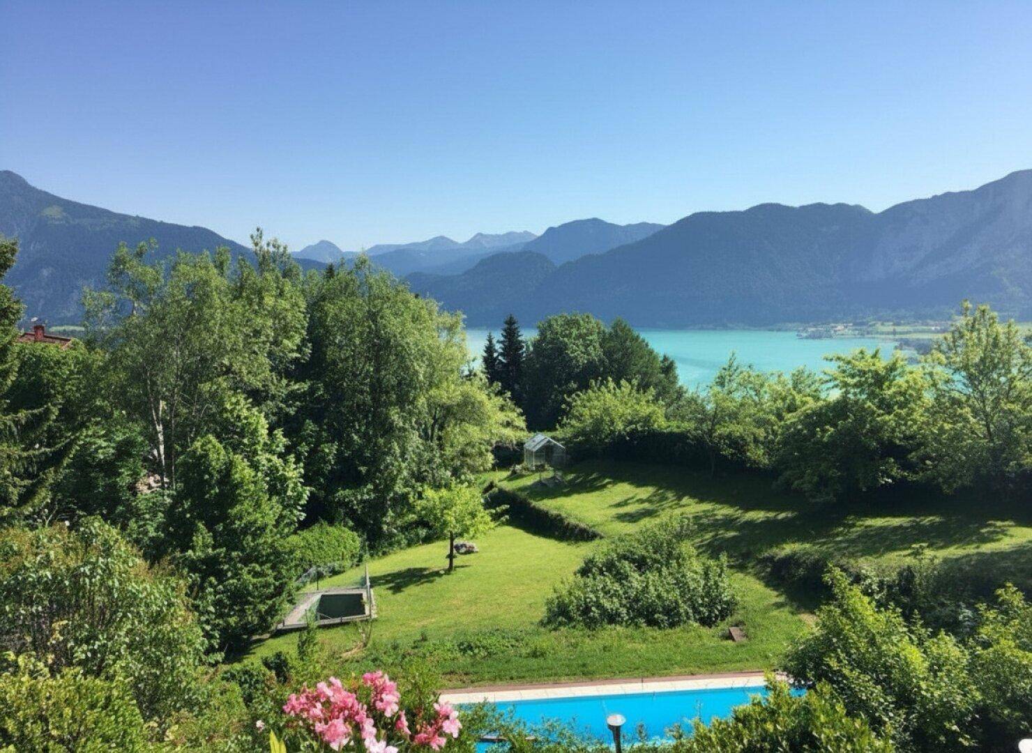 Grüner Garten mit Pool und weitem Blick auf den türkisfarbenen See und die Berge.