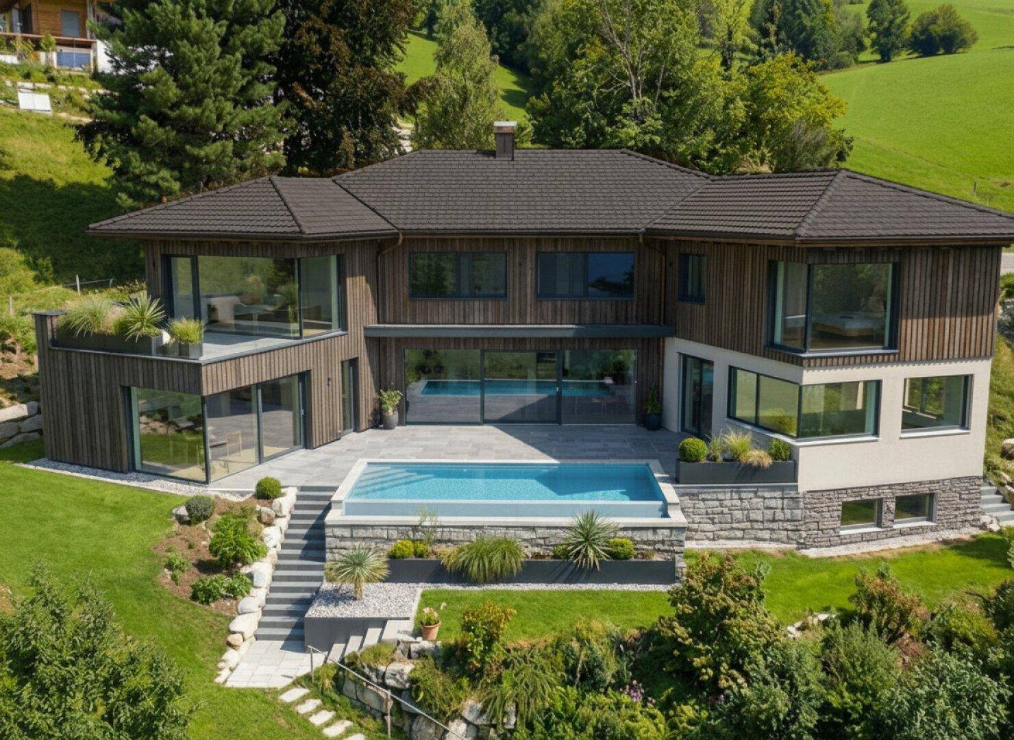 Moderne Villa mit großzügigen Glasfronten und Außenpool, eingebettet in grüne Hügellandschaft.