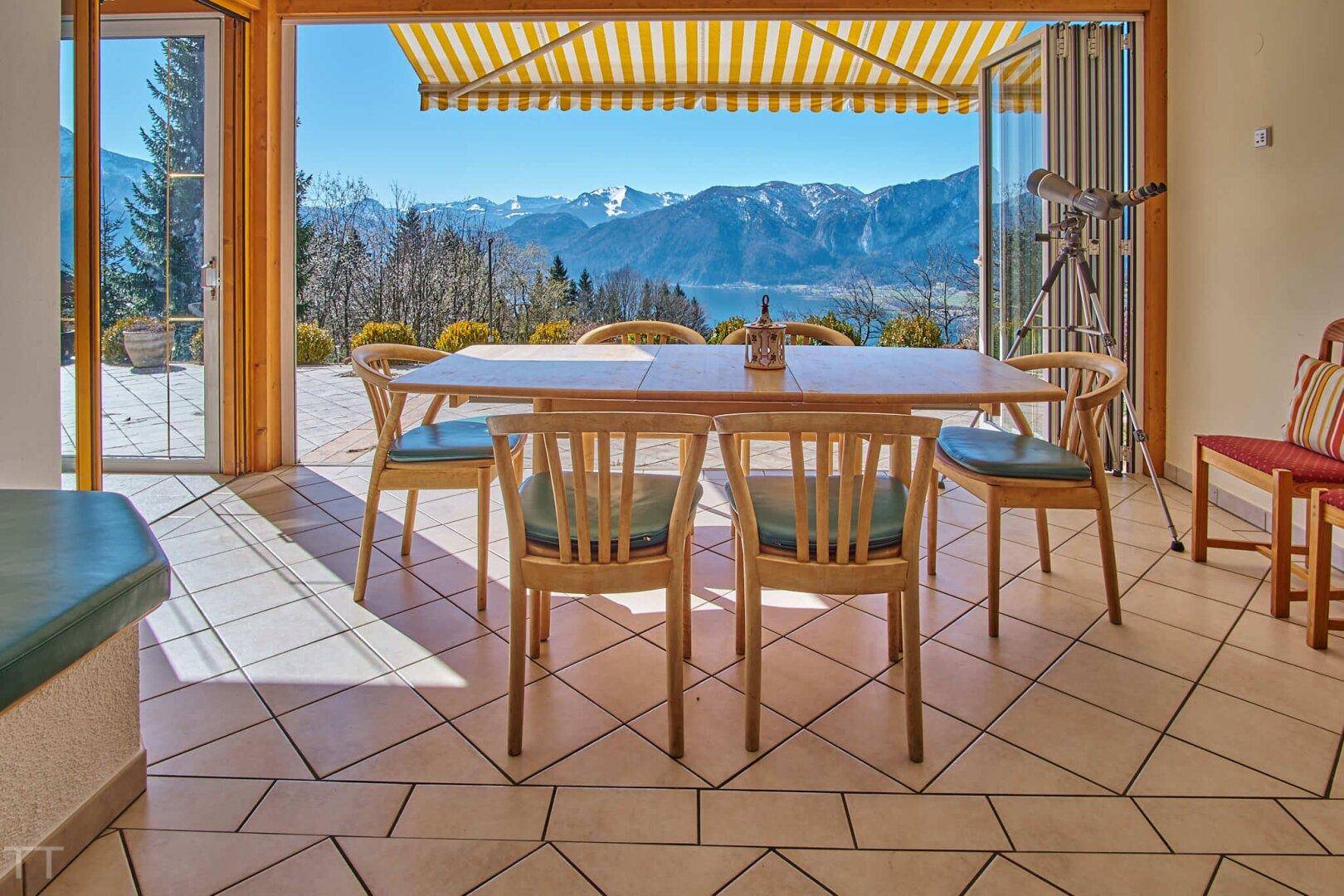 Heller Essbereich mit Holztisch, Fliesenboden und Zugang zur Terrasse mit Bergblick.