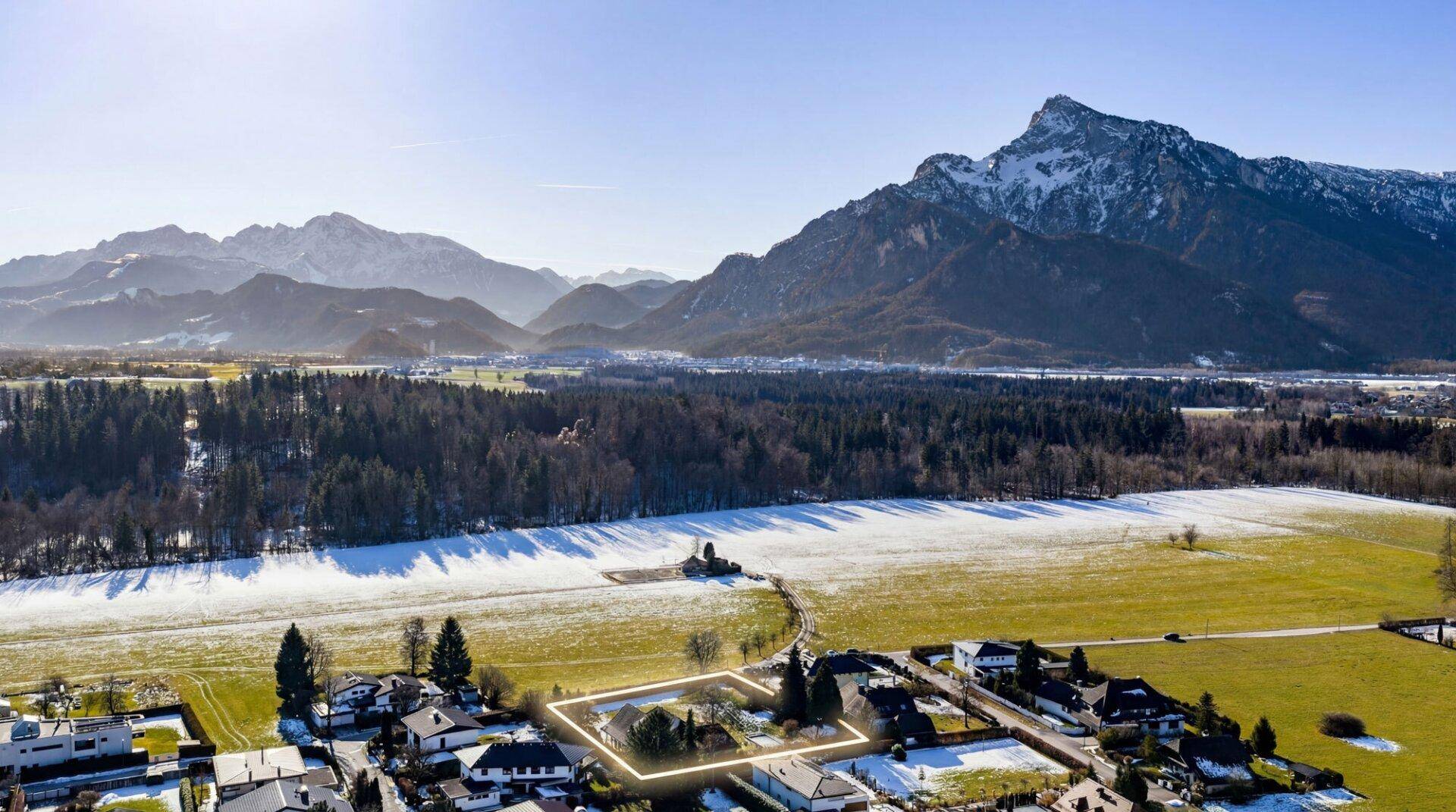 Luftaufnahme eines Grundstücks in ländlicher Umgebung mit Bergen und teilweise schneebedeckten Feldern.