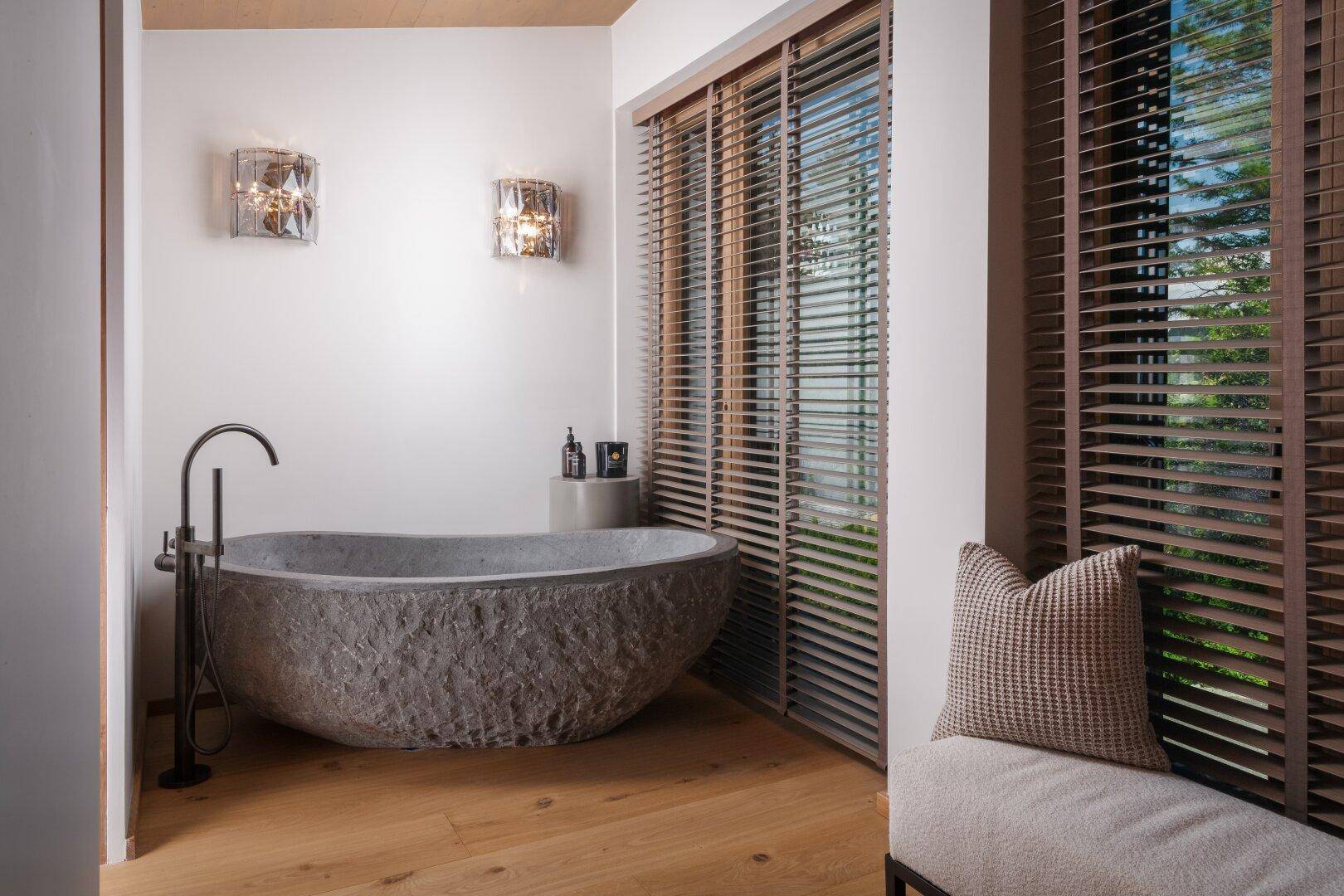 Elegantes Badezimmer mit freistehender Steinbadewanne, Holzjalousien und Holzboden.